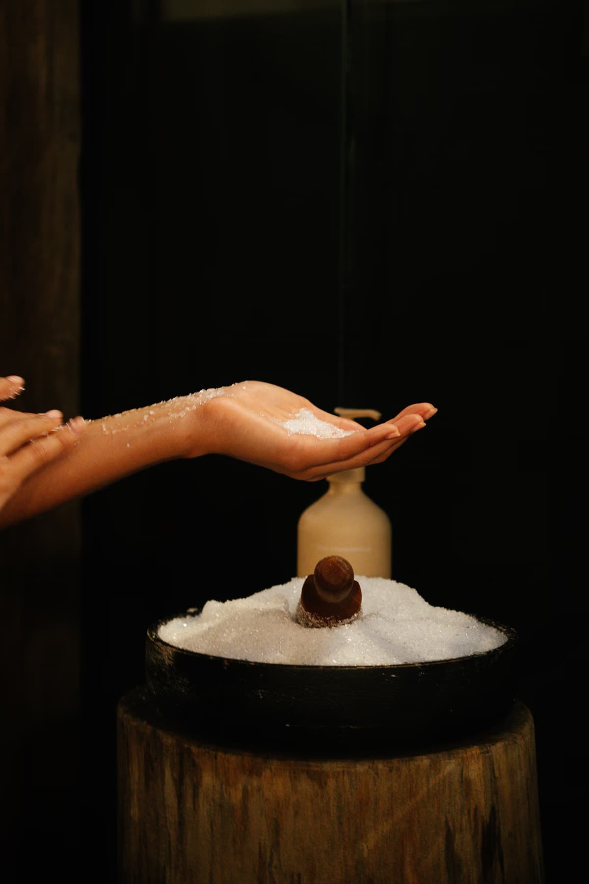 Hands cupping bath salts beside an amber bottle on a timber stand at Navia Bathhouse